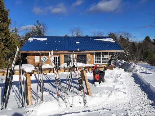 A wooden building with a blue roof surrounded by snow, featuring ski equipment outside and a clear blue sky.
