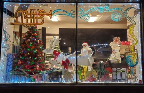 A festive shop window displays a decorated Christmas tree, a reindeer, and holiday gifts with colorful lights.