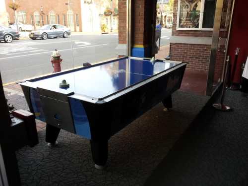 A blue air hockey table sits near a window, with a street view and a fire hydrant visible outside.