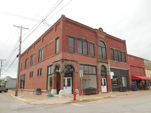 Historic red brick building with large windows, decorative arches, and a corner entrance, set on a quiet street.