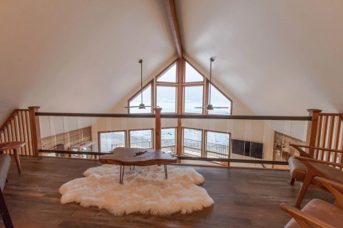 Cozy loft space with large windows, wooden railing, and a plush rug, offering a scenic view of the outdoors.