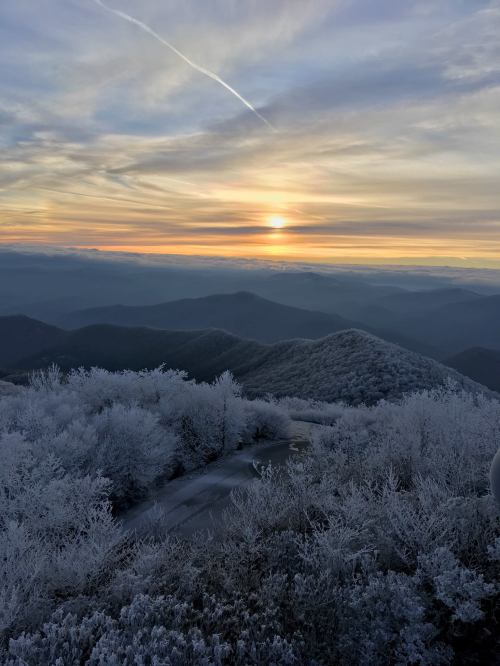 A stunning sunrise over frosted mountains, with a winding road and a colorful sky in the background.