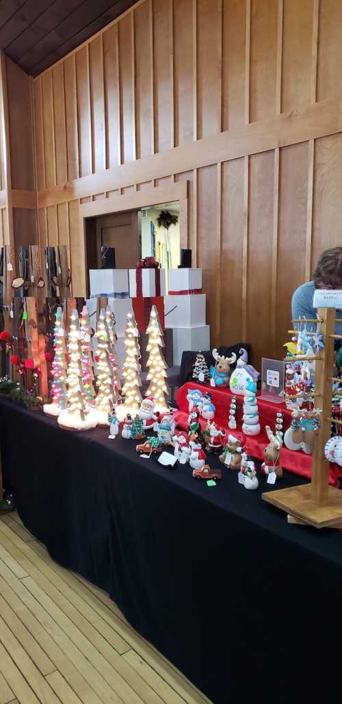 A festive display of handmade holiday decorations, including trees, snowmen, and other ornaments on a black table.