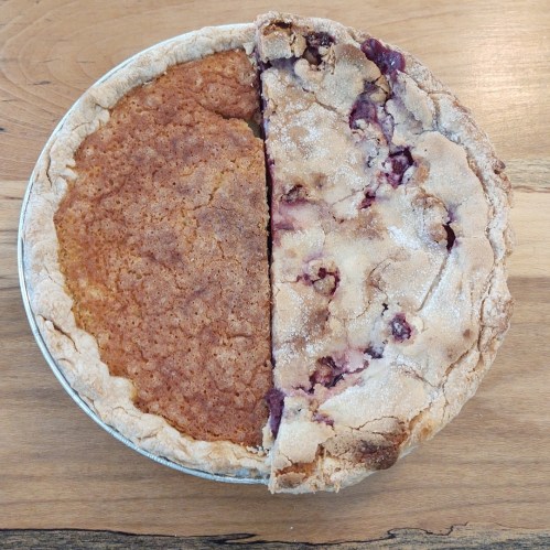 A pie with a golden brown crust, half filled with a cherry filling and half with a light brown, cake-like texture.