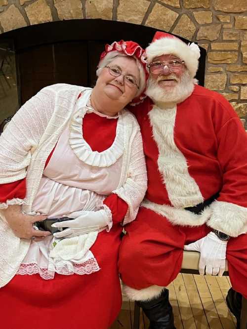 A cheerful Santa Claus and Mrs. Claus pose together, both dressed in traditional holiday attire, smiling warmly.