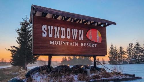 Sign for Sundown Mountain Resort at sunrise, surrounded by snow and trees.
