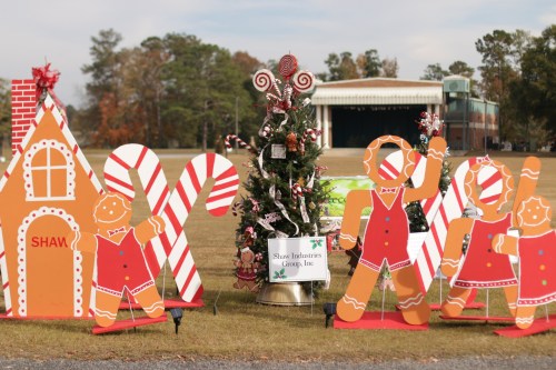 Colorful holiday decorations featuring gingerbread figures, candy canes, and a decorated tree in a festive outdoor setting.