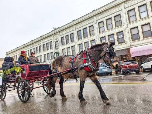 A horse-drawn carriage with passengers rides down a snowy street lined with historic buildings.