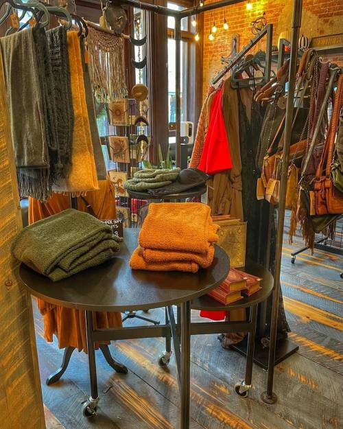 A cozy boutique display featuring folded blankets, clothing racks, and warm lighting against a rustic brick backdrop.