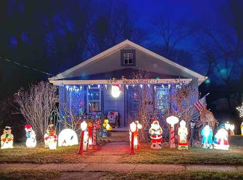 A cozy house decorated with colorful Christmas lights and festive lawn decorations, including snowmen and Santa figures.