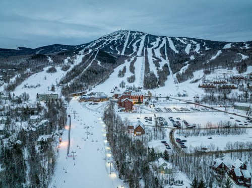 A snowy mountain landscape with ski slopes, a resort, and chairlifts under a cloudy sky.