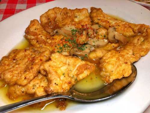 A plate of golden fried fish fillets topped with a savory sauce and garnished with herbs.