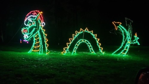 A colorful light display of a dragon wearing a Santa hat, set against a dark, rainy background.