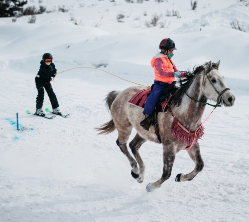A child on a horse pulls a skier through snowy terrain, showcasing a fun winter activity.