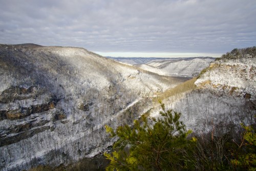 Snow-covered mountains and valleys under a cloudy sky, showcasing a serene winter landscape.