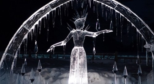 A stunning ice sculpture of a woman with a crown, surrounded by icicles, set against a dark background.