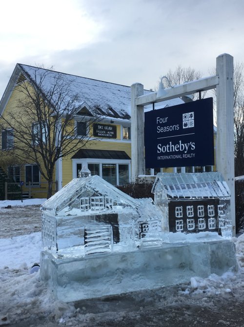 Ice sculpture of houses in front of a real estate sign for Four Seasons Sotheby's, with a snowy background.
