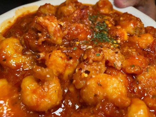 A close-up of a plate of gnocchi in a rich tomato sauce, garnished with herbs and spices.