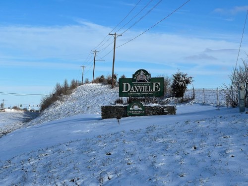 A snowy landscape featuring a green sign for Danville, with power lines and a clear blue sky in the background.