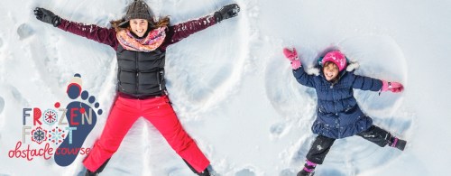 A woman and a child lying in the snow, making snow angels, with colorful winter clothing and a playful atmosphere.