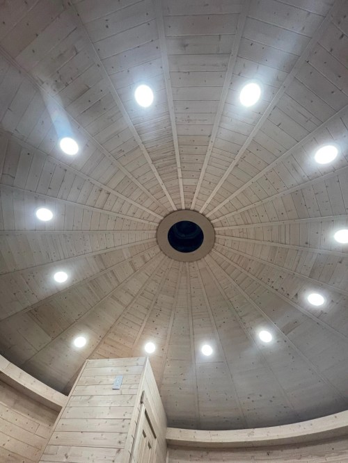 Interior view of a circular wooden ceiling with recessed lights, featuring a central circular opening.