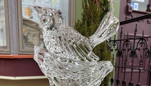 A detailed ice sculpture of a bird perched on a branch, displayed outdoors near a building.