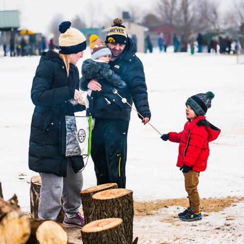 A family enjoys a snowy day outdoors, with a child holding a string and adults interacting nearby.