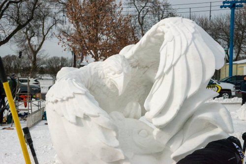 A large snow sculpture of an eagle with outstretched wings, perched over a fish, set in a snowy landscape.