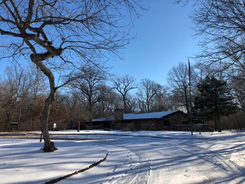 A snow-covered landscape featuring a stone building, trees, and a clear blue sky.