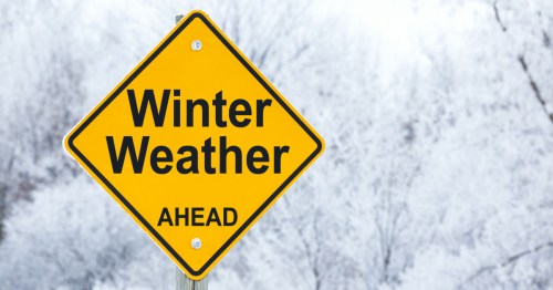 A yellow warning sign that reads "Winter Weather Ahead" against a snowy, frosted background.