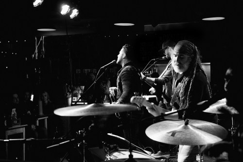 A black and white photo of a live band performing on stage, with musicians singing and playing instruments.