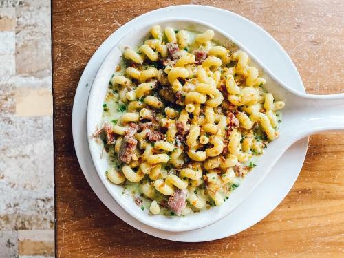 A bowl of creamy pasta with curly noodles, topped with crispy bits and herbs, served on a wooden table.
