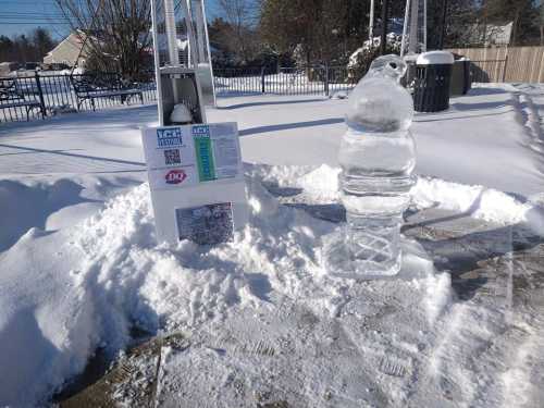 An ice sculpture resembling a soft serve cone stands in a snowy area next to a sign and a snow-covered ground.