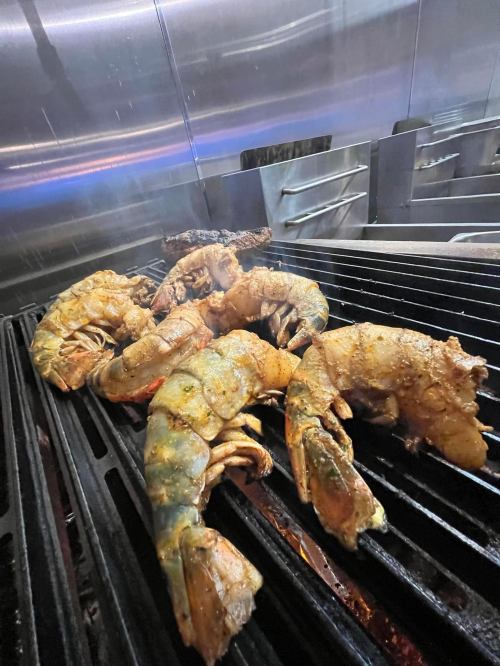 Grilled shrimp and lobster tails cooking on a barbecue grill with a shiny metal background.