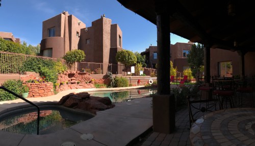 A serene courtyard with a pool, surrounded by adobe-style buildings and lush greenery under a clear blue sky.