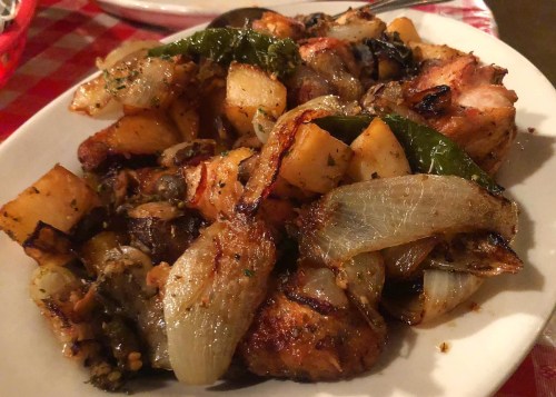 A plate of roasted chicken with potatoes, onions, and green peppers, garnished with herbs.
