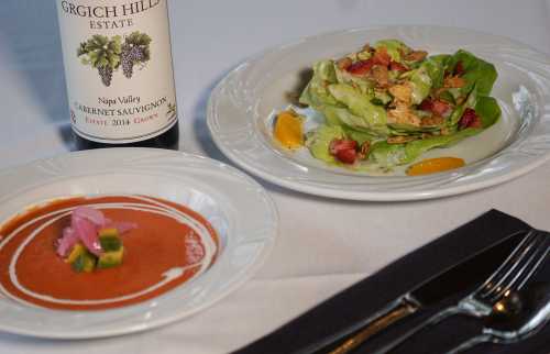 A plate with a salad, a bowl of soup, and a bottle of Grgich Hills Estate wine on a white tablecloth.