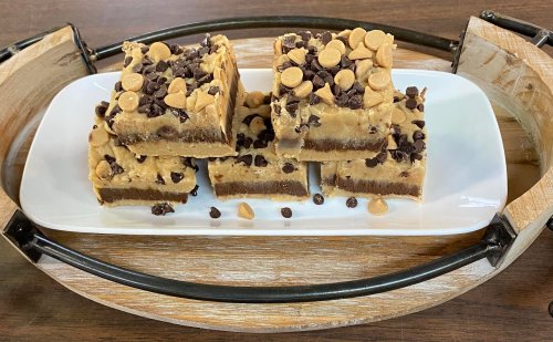 A plate of layered dessert bars topped with chocolate and butterscotch chips, arranged on a wooden tray.