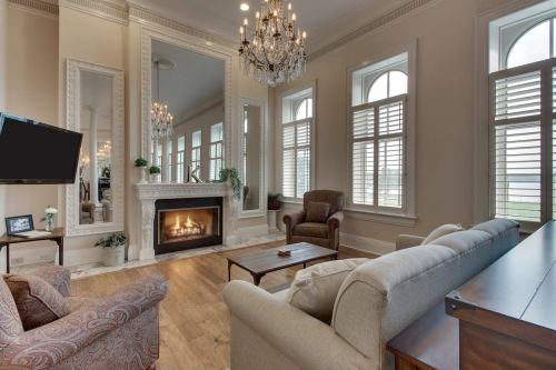 Elegant living room with a fireplace, large mirrors, chandeliers, and comfortable seating. Bright, airy atmosphere.