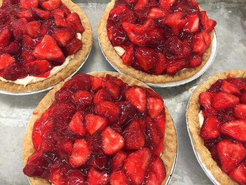 Four strawberry pies with a glossy red glaze and a golden crust, filled with fresh strawberries on a creamy base.