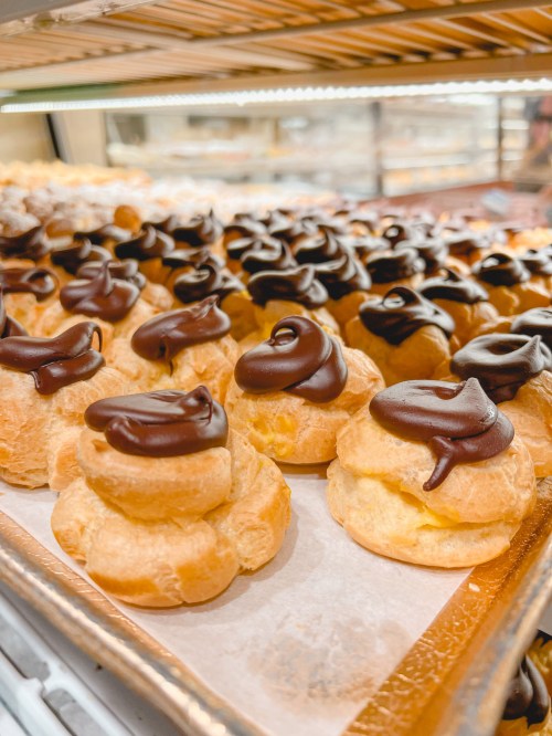 A display of cream puffs topped with chocolate frosting, arranged neatly on a tray.