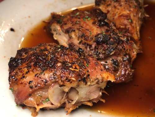 Close-up of juicy, roasted chicken pieces with crispy skin, served in a flavorful sauce on a white plate.