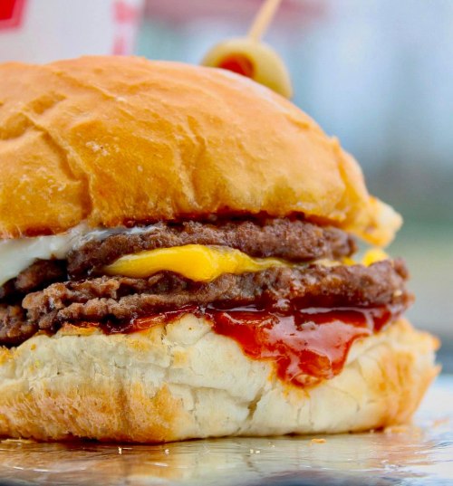 A close-up of a juicy hamburger with two beef patties, melted cheese, and ketchup on a soft bun.