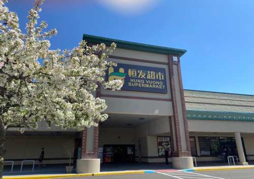 Exterior of Hung Vuong Supermarket with blooming trees in front and a clear blue sky.