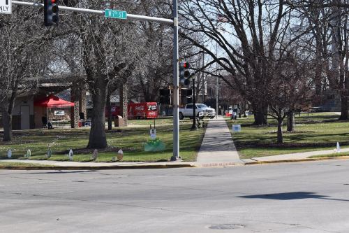 A park scene with traffic lights, a sidewalk, and tents in the background, surrounded by bare trees.