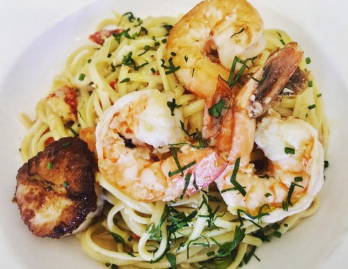 A plate of linguine topped with shrimp, scallops, and fresh herbs.