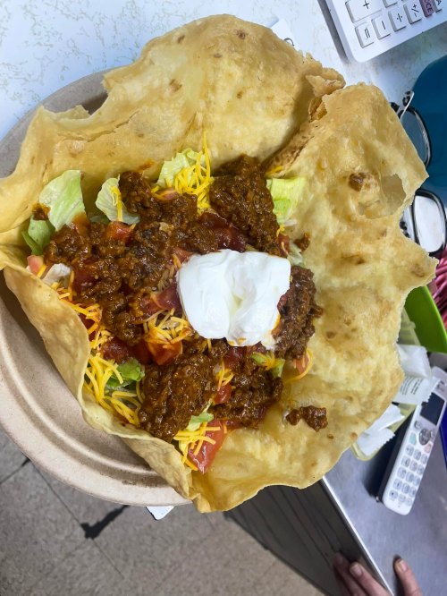 A large taco bowl filled with lettuce, tomatoes, cheese, and topped with chili and a dollop of sour cream.