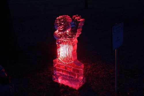 An illuminated ice sculpture of a rooster, glowing red against a dark background.