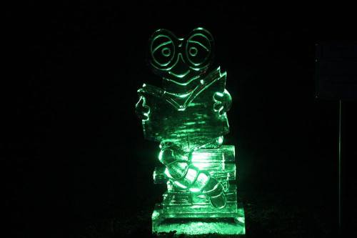 A glowing green ice sculpture of a character reading a book, sitting on a stack of books.