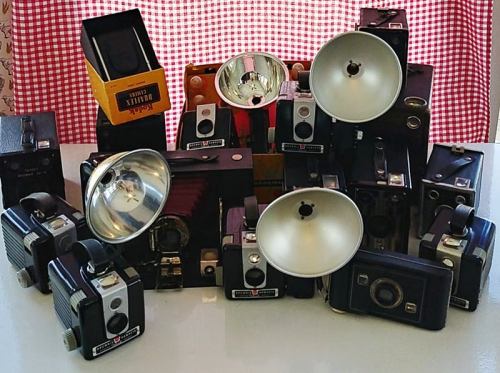 A collection of vintage cameras and lighting equipment arranged on a table, with a checkered background.